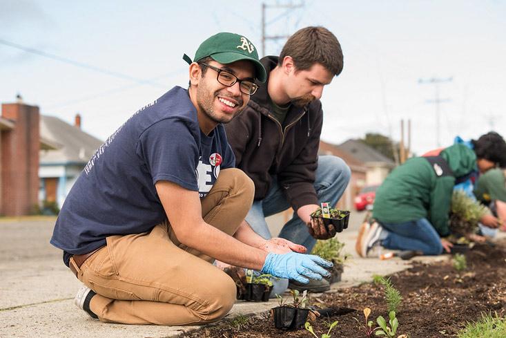 Two students planting and one smiling for the camera